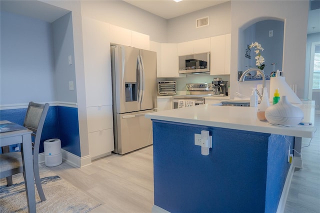 3406 Soho St Unit 102, Orlando, FL 32835 - kitchen featuring appliances with stainless steel finishes, a peninsula, light countertops, light wood-type flooring, and white cabinets