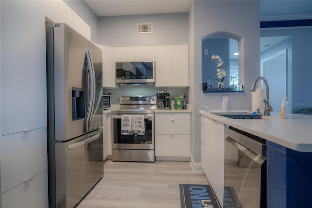 kitchen featuring ornamental molding, stainless steel appliances, sink, white cabinets, and light hardwood / wood-style floors