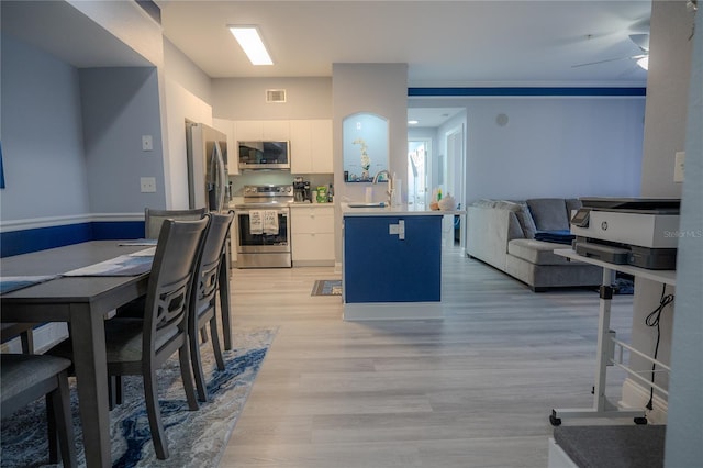 kitchen with appliances with stainless steel finishes, light wood-type flooring, ceiling fan, sink, and white cabinetry