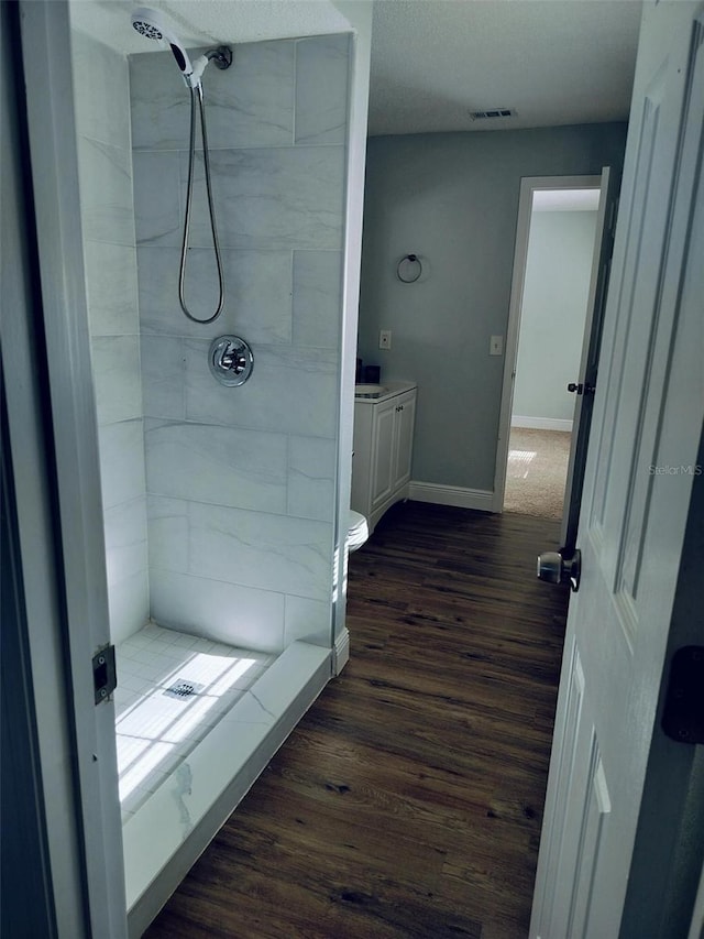 bathroom with hardwood / wood-style floors, vanity, toilet, and tiled shower