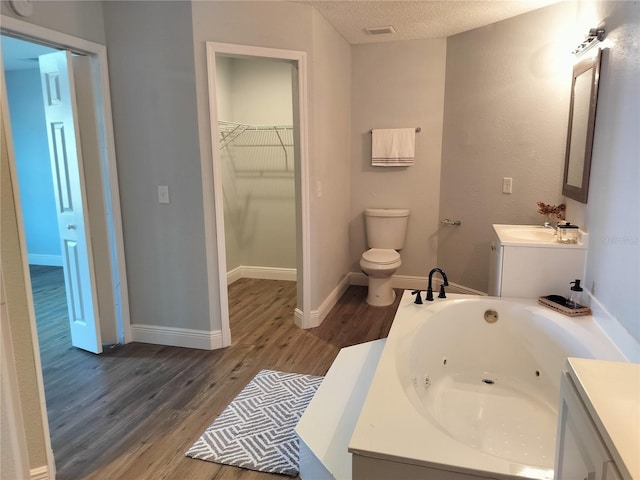 bathroom with a bathtub, vanity, a textured ceiling, hardwood / wood-style floors, and toilet