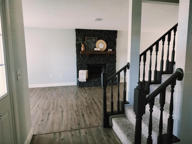 stairway featuring a textured ceiling, wood-type flooring, and a fireplace