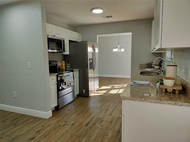 kitchen with appliances with stainless steel finishes, light wood-type flooring, sink, white cabinetry, and hanging light fixtures