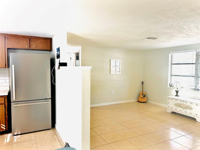 kitchen with decorative backsplash, a textured ceiling, light tile patterned floors, and stainless steel refrigerator