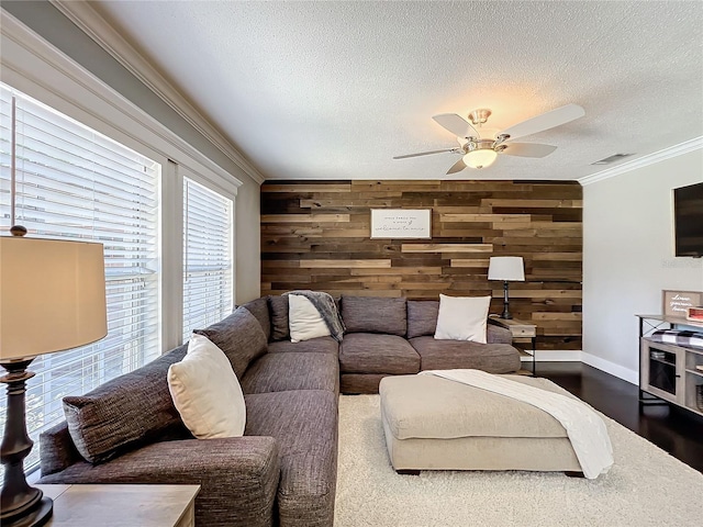 living room with wood walls, crown molding, ceiling fan, a textured ceiling, and wood-type flooring