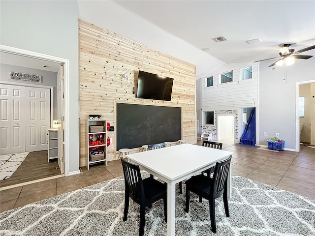 dining space featuring tile patterned floors, ceiling fan, lofted ceiling, and wooden walls