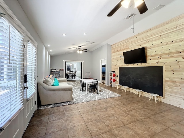 tiled living room with ceiling fan, lofted ceiling, and wood walls