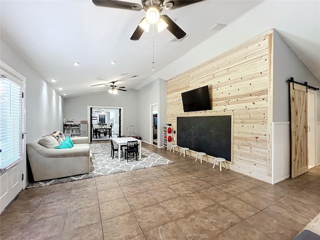 unfurnished living room with a barn door, wooden walls, ceiling fan, and vaulted ceiling