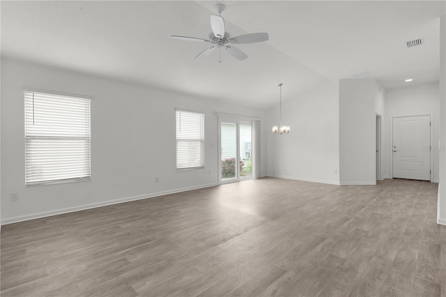 spare room with ceiling fan with notable chandelier, light hardwood / wood-style floors, and lofted ceiling