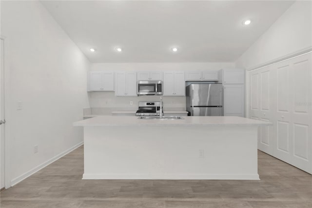 kitchen featuring an island with sink, stainless steel appliances, vaulted ceiling, and light hardwood / wood-style floors