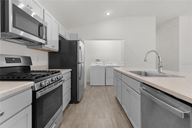 kitchen with lofted ceiling, sink, washer and dryer, appliances with stainless steel finishes, and light hardwood / wood-style floors