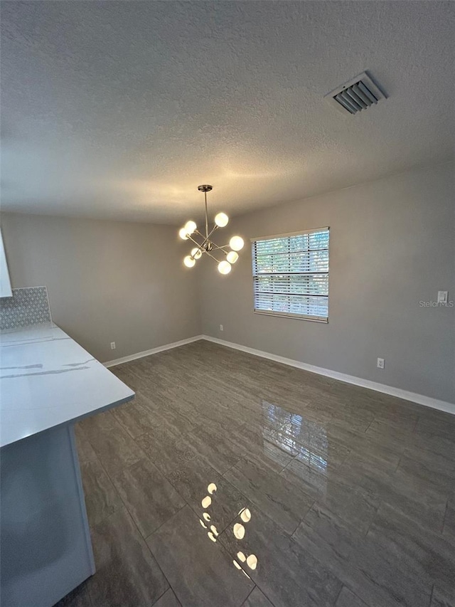 unfurnished dining area featuring a textured ceiling and an inviting chandelier