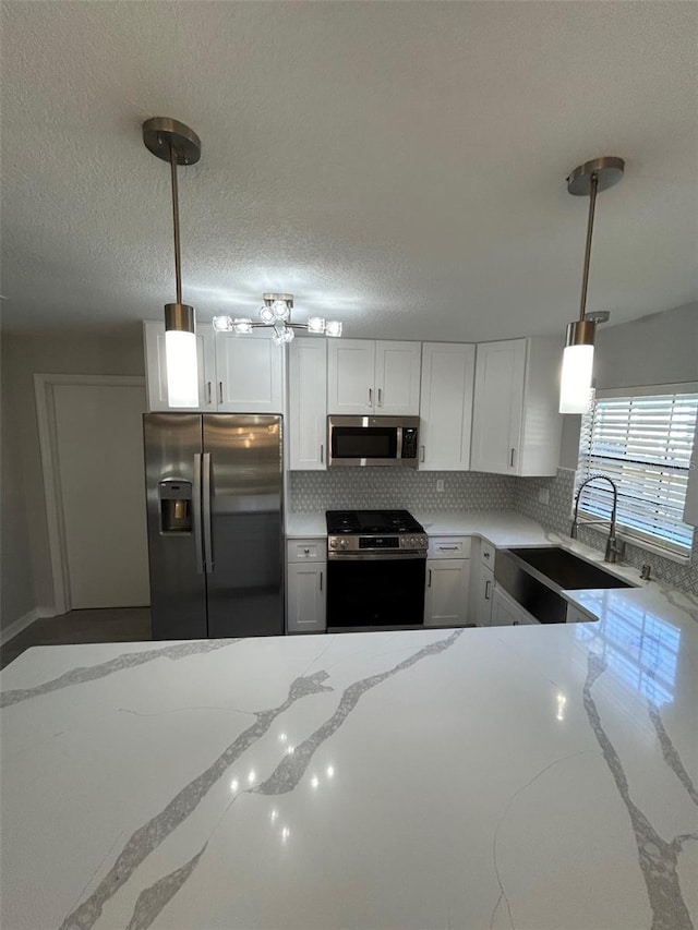 kitchen featuring appliances with stainless steel finishes, light stone counters, sink, decorative light fixtures, and white cabinets