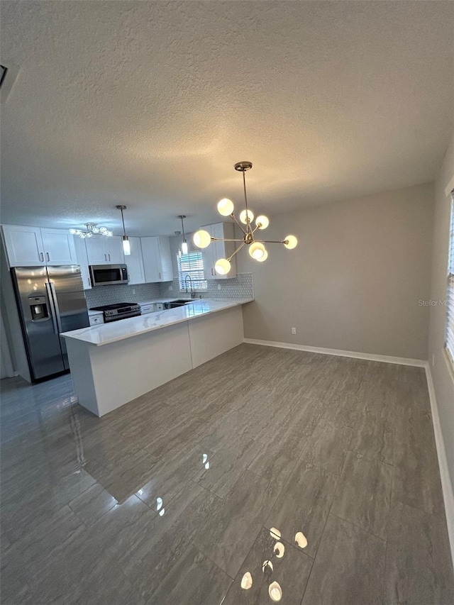 kitchen with a peninsula, a textured ceiling, baseboards, a notable chandelier, and appliances with stainless steel finishes