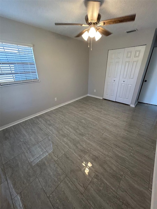 unfurnished bedroom featuring a textured ceiling, visible vents, baseboards, and ceiling fan