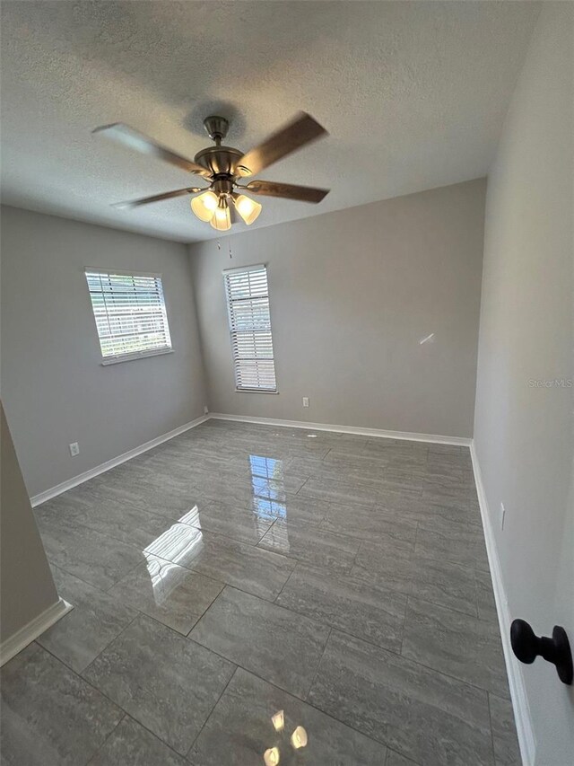 empty room with a textured ceiling, a ceiling fan, and baseboards