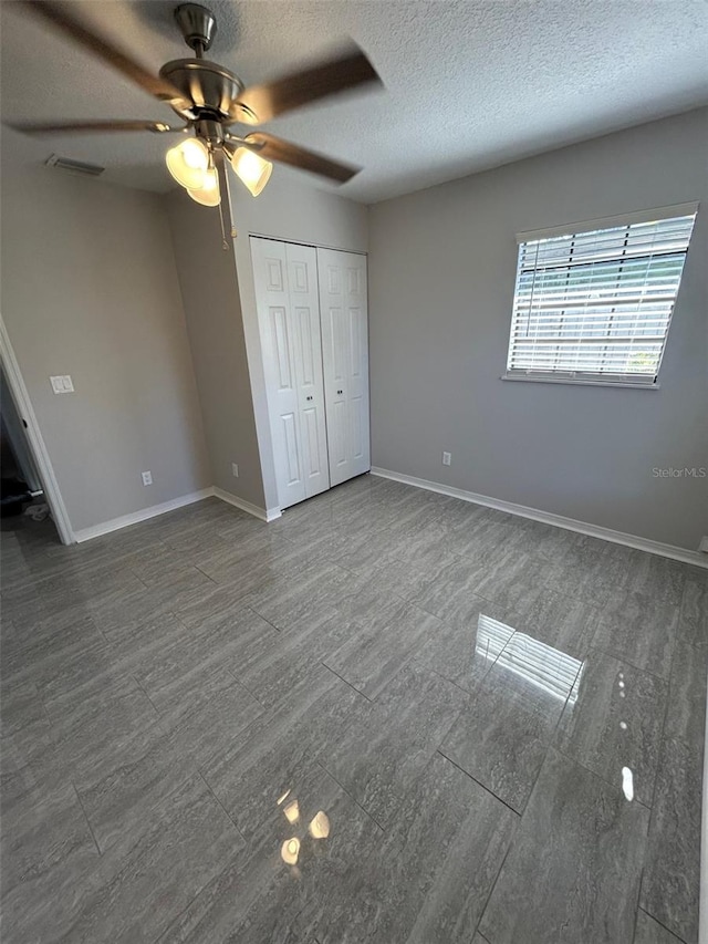 unfurnished bedroom featuring a textured ceiling, baseboards, visible vents, a closet, and ceiling fan