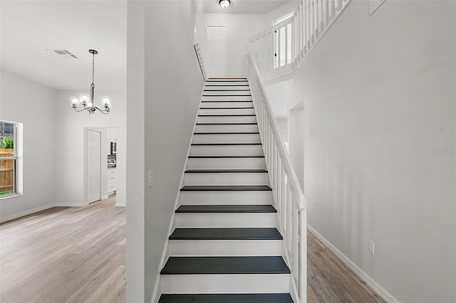 staircase with hardwood / wood-style flooring, a notable chandelier, and a high ceiling