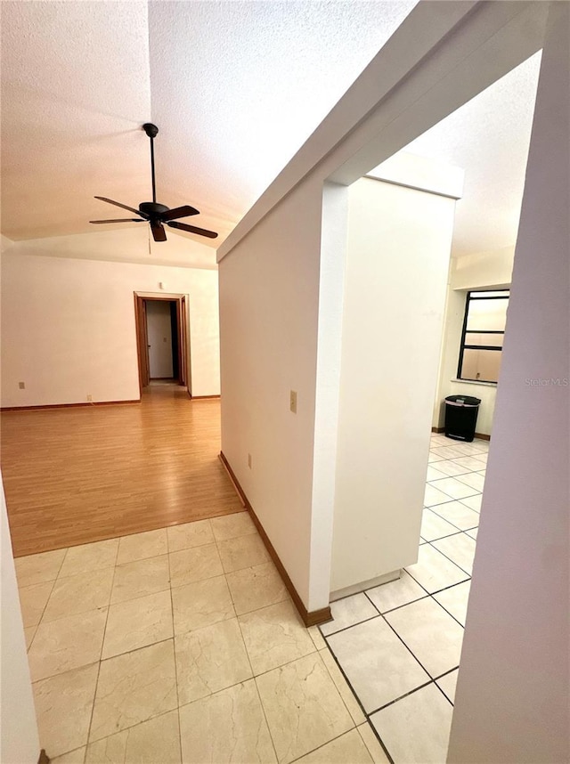 hall featuring light hardwood / wood-style floors, a textured ceiling, and vaulted ceiling