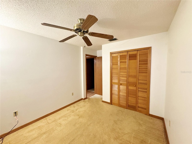 unfurnished bedroom featuring light carpet, a textured ceiling, a closet, and ceiling fan