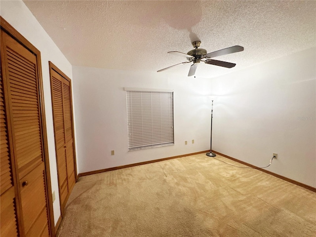 unfurnished bedroom featuring a textured ceiling, light colored carpet, ceiling fan, and multiple closets