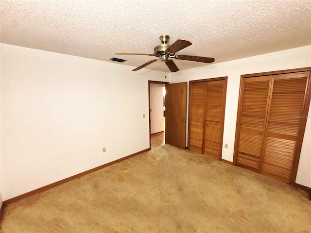 unfurnished bedroom featuring multiple closets, ceiling fan, light colored carpet, and a textured ceiling