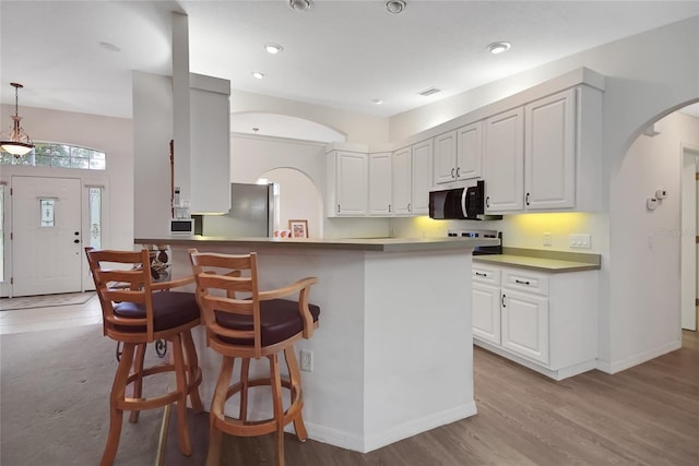 kitchen with white cabinets, decorative light fixtures, light wood-type flooring, and stainless steel appliances