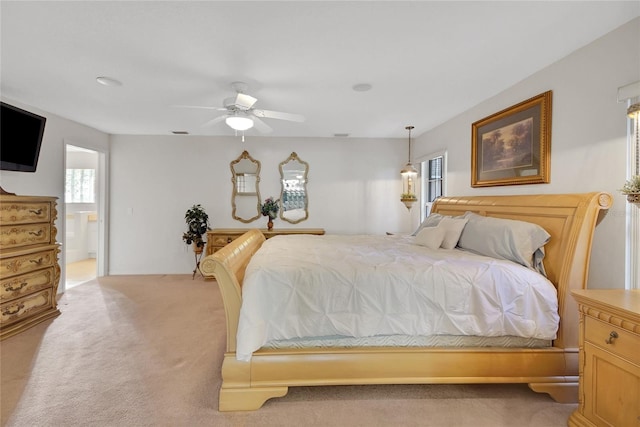 bedroom featuring multiple windows, ceiling fan, ensuite bathroom, and light carpet