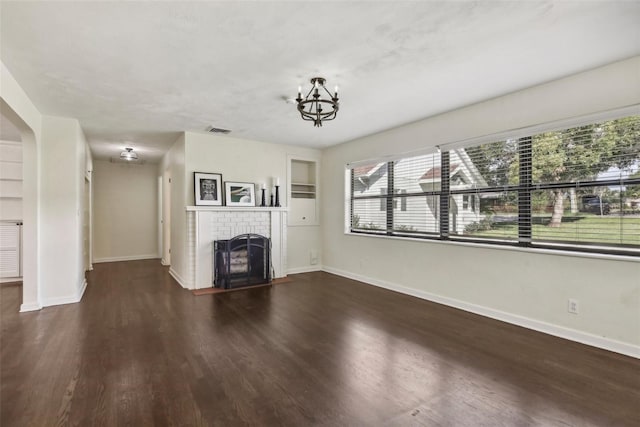 unfurnished living room with a chandelier, dark hardwood / wood-style flooring, and a brick fireplace