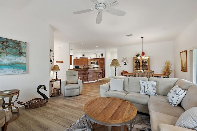 living room with ceiling fan with notable chandelier and light wood-type flooring