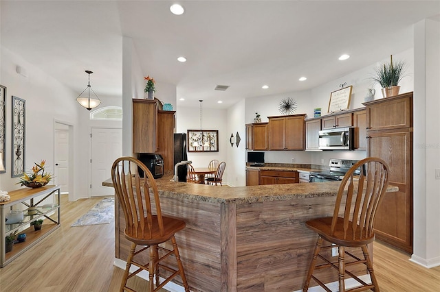 kitchen with kitchen peninsula, appliances with stainless steel finishes, light wood-type flooring, and hanging light fixtures