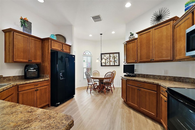 kitchen with stone countertops, black appliances, decorative light fixtures, and light wood-type flooring