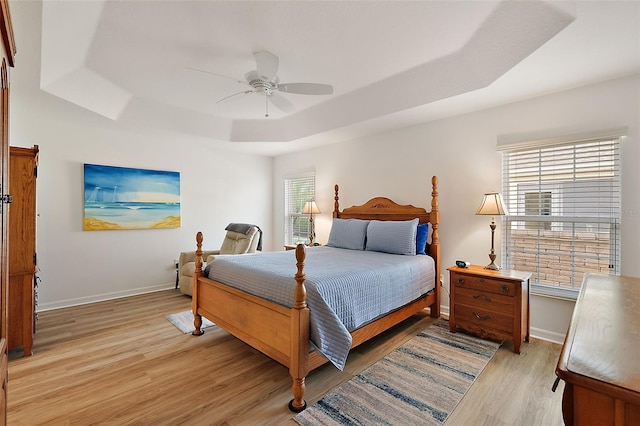 bedroom with a raised ceiling, multiple windows, ceiling fan, and light hardwood / wood-style flooring