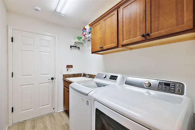 laundry room with cabinets, light wood-type flooring, a textured ceiling, sink, and washing machine and clothes dryer