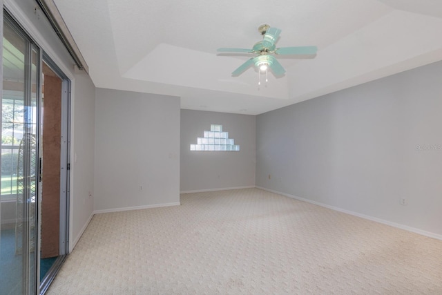 carpeted spare room featuring a raised ceiling, ceiling fan, and a healthy amount of sunlight