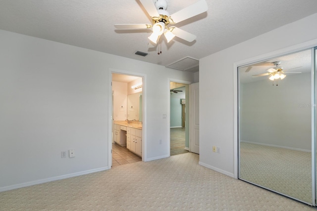 unfurnished bedroom with a textured ceiling, ceiling fan, light colored carpet, and ensuite bathroom