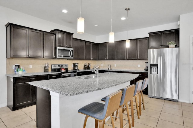 kitchen with a breakfast bar, a center island with sink, sink, appliances with stainless steel finishes, and decorative light fixtures