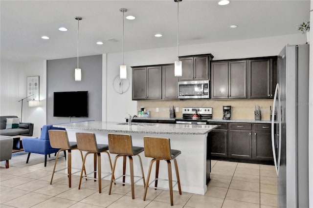 kitchen with appliances with stainless steel finishes, light stone counters, a kitchen island with sink, decorative light fixtures, and a breakfast bar area