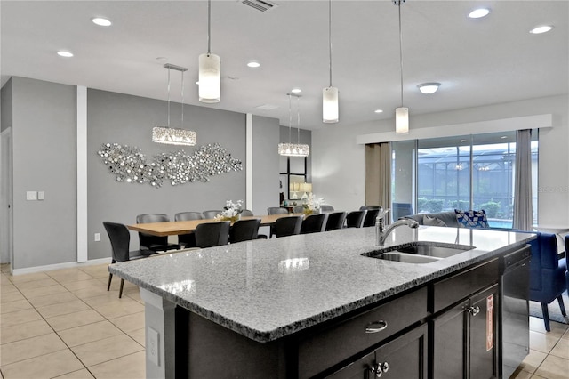 kitchen featuring dishwasher, hanging light fixtures, light stone counters, an island with sink, and light tile patterned flooring