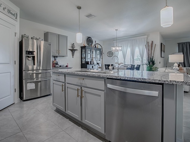 kitchen featuring light stone countertops, appliances with stainless steel finishes, a center island with sink, gray cabinets, and hanging light fixtures