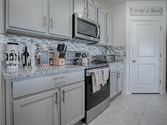 kitchen with backsplash, gray cabinets, light stone countertops, light tile patterned floors, and stainless steel appliances