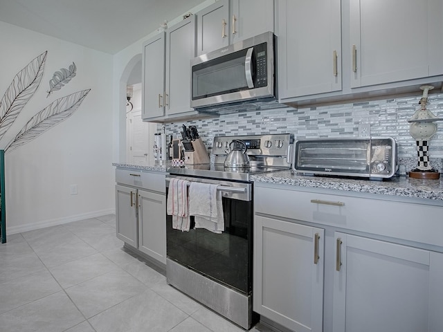 kitchen with tasteful backsplash, light stone countertops, light tile patterned floors, and stainless steel appliances