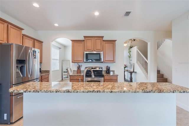 kitchen with stainless steel appliances, light tile patterned floors, a kitchen island with sink, and light stone countertops