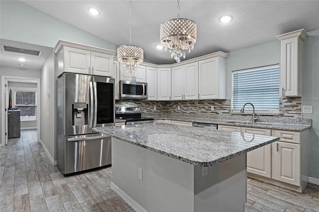 kitchen featuring sink, pendant lighting, vaulted ceiling, a kitchen island, and appliances with stainless steel finishes