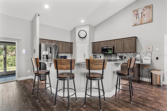 kitchen with appliances with stainless steel finishes, dark hardwood / wood-style flooring, a kitchen island, a kitchen bar, and dark brown cabinetry