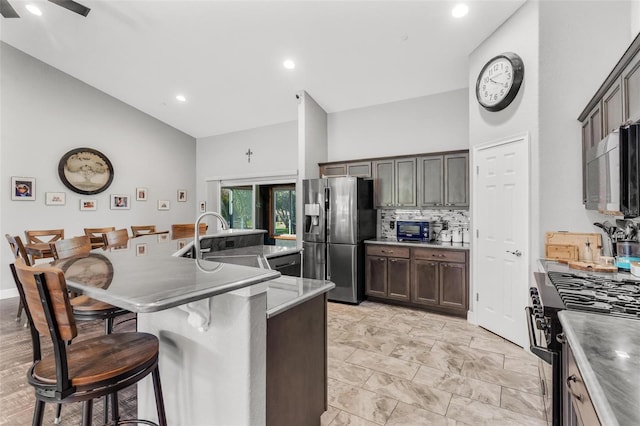 kitchen featuring sink, stainless steel appliances, high vaulted ceiling, a kitchen bar, and a kitchen island