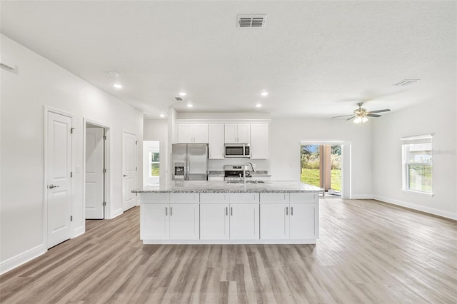 kitchen with white cabinets, light wood-type flooring, a kitchen island with sink, and appliances with stainless steel finishes