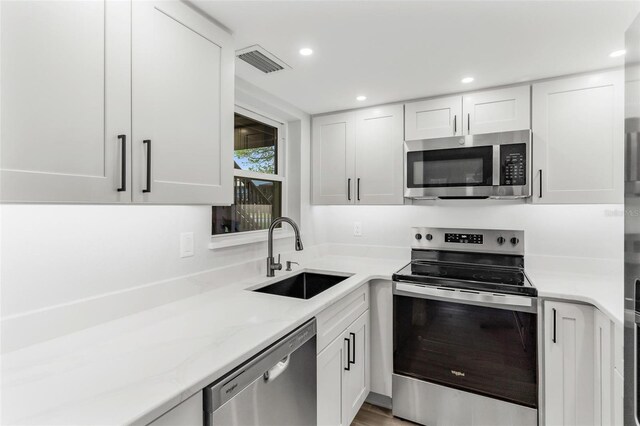 kitchen featuring white cabinets, sink, light stone countertops, light wood-type flooring, and stainless steel appliances