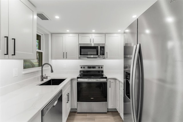 kitchen with light hardwood / wood-style flooring, appliances with stainless steel finishes, sink, white cabinets, and light stone countertops