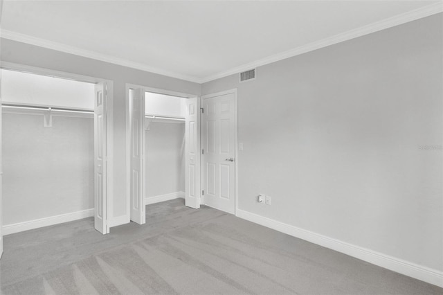 unfurnished bedroom featuring crown molding, light colored carpet, and two closets